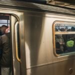 Trump administration threatens to cut New York transit funds over safety - A packed New York City subway train with passengers standing tightly together during a busy commute. The train doors remain open as people continue boarding, reflecting the high density and pace of daily transit in NYC. The scene captures the intensity of rush hour in the MTA system and the collective rhythm of urban life in one of the busiest subway networks in the world.