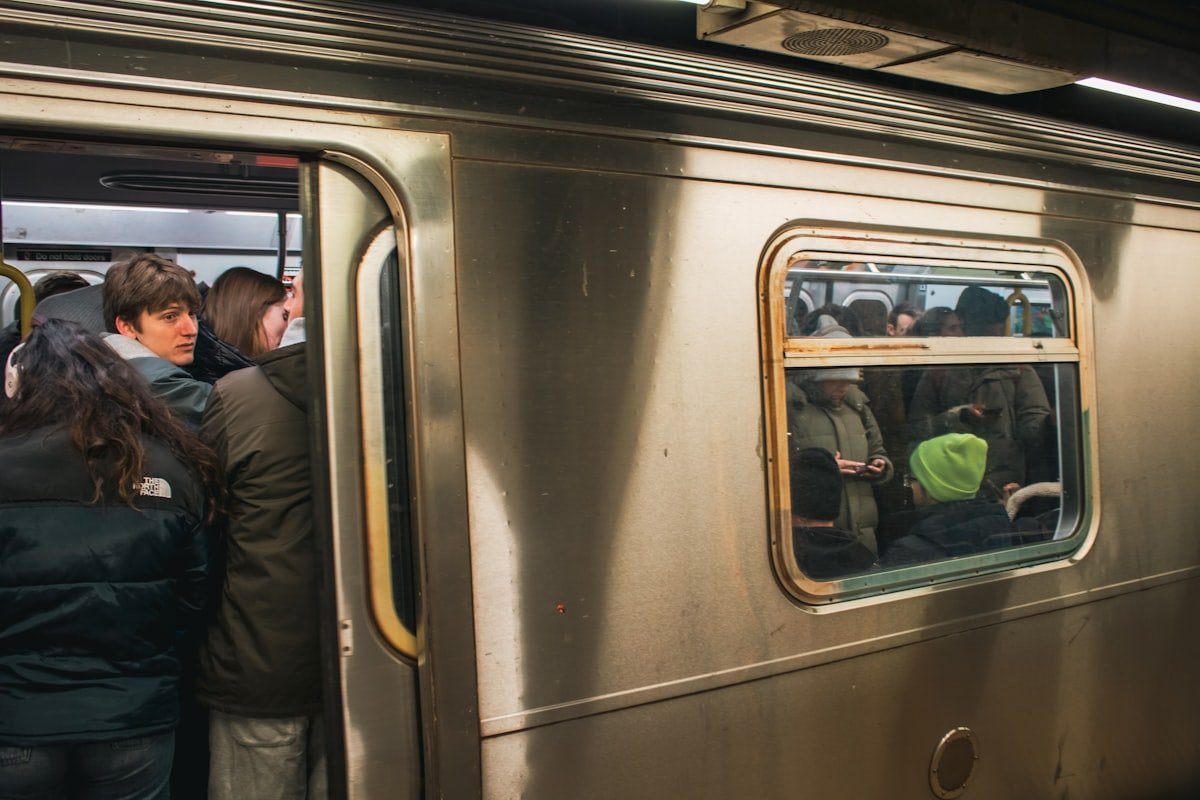 Trump administration threatens to cut New York transit funds over safety - A packed New York City subway train with passengers standing tightly together during a busy commute. The train doors remain open as people continue boarding, reflecting the high density and pace of daily transit in NYC. The scene captures the intensity of rush hour in the MTA system and the collective rhythm of urban life in one of the busiest subway networks in the world.